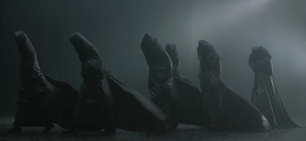 'Dune' (2021) screenshot showing the completely covered Bene Gesserit group moving against the wind and rain.