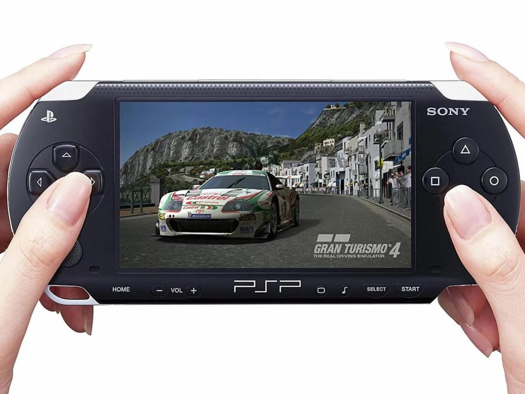 A pair of hands holding a PSP with 'Gran Turismo 4' playing on it.